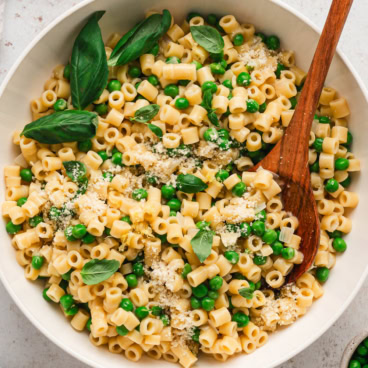 Square image of pasta and peas in a white serving bowl.