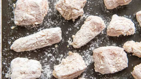 Flour coated pieces of chicken on a baking tray.
