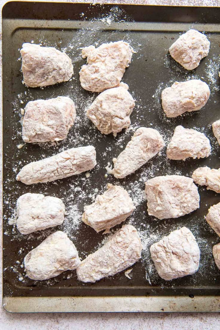 Flour coated pieces of chicken on a baking tray.