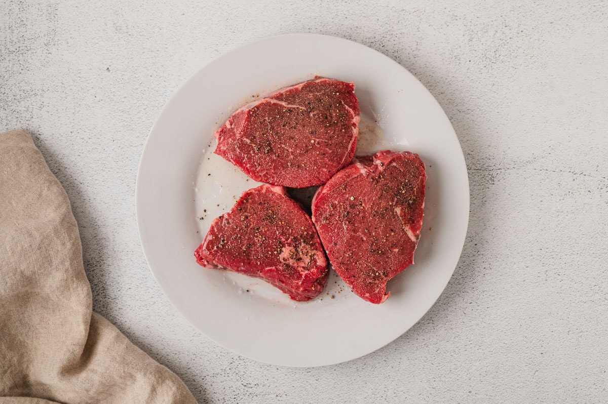 Raw steaks on a white plate.