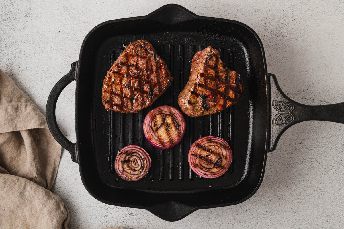 Grilled steaks and onions on a grill plan.