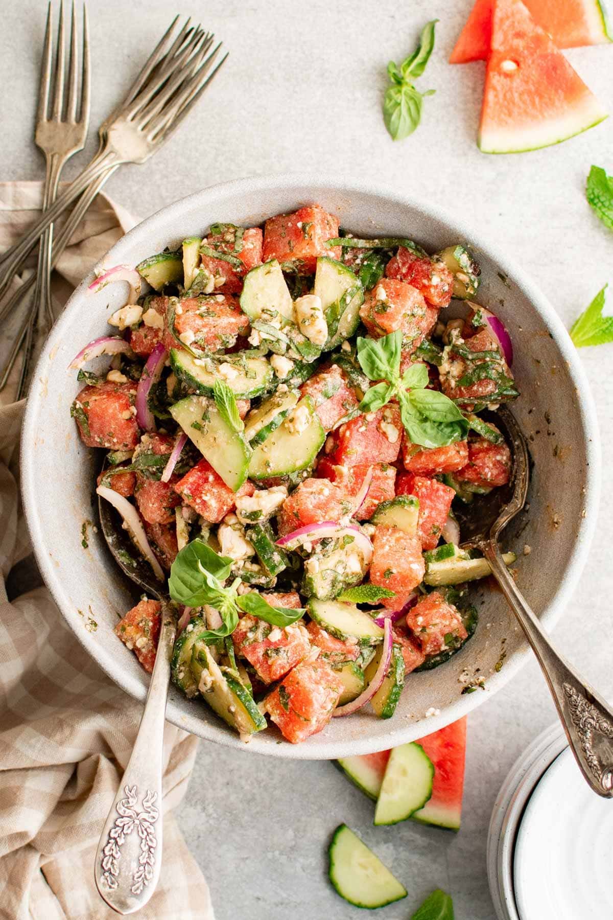 Large bowl of watermelon salad with silver serving spoons.