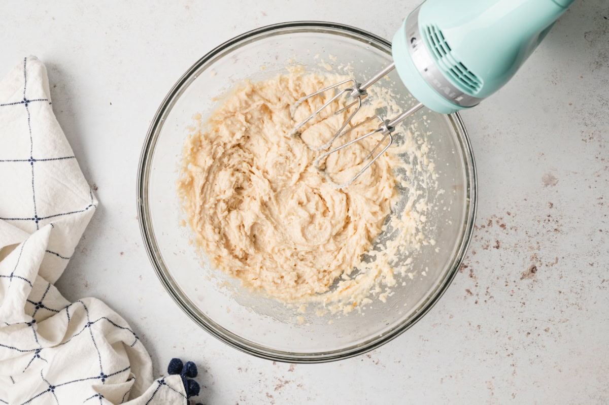 Yellow batter mixture in a bowl with a hand mixer.
