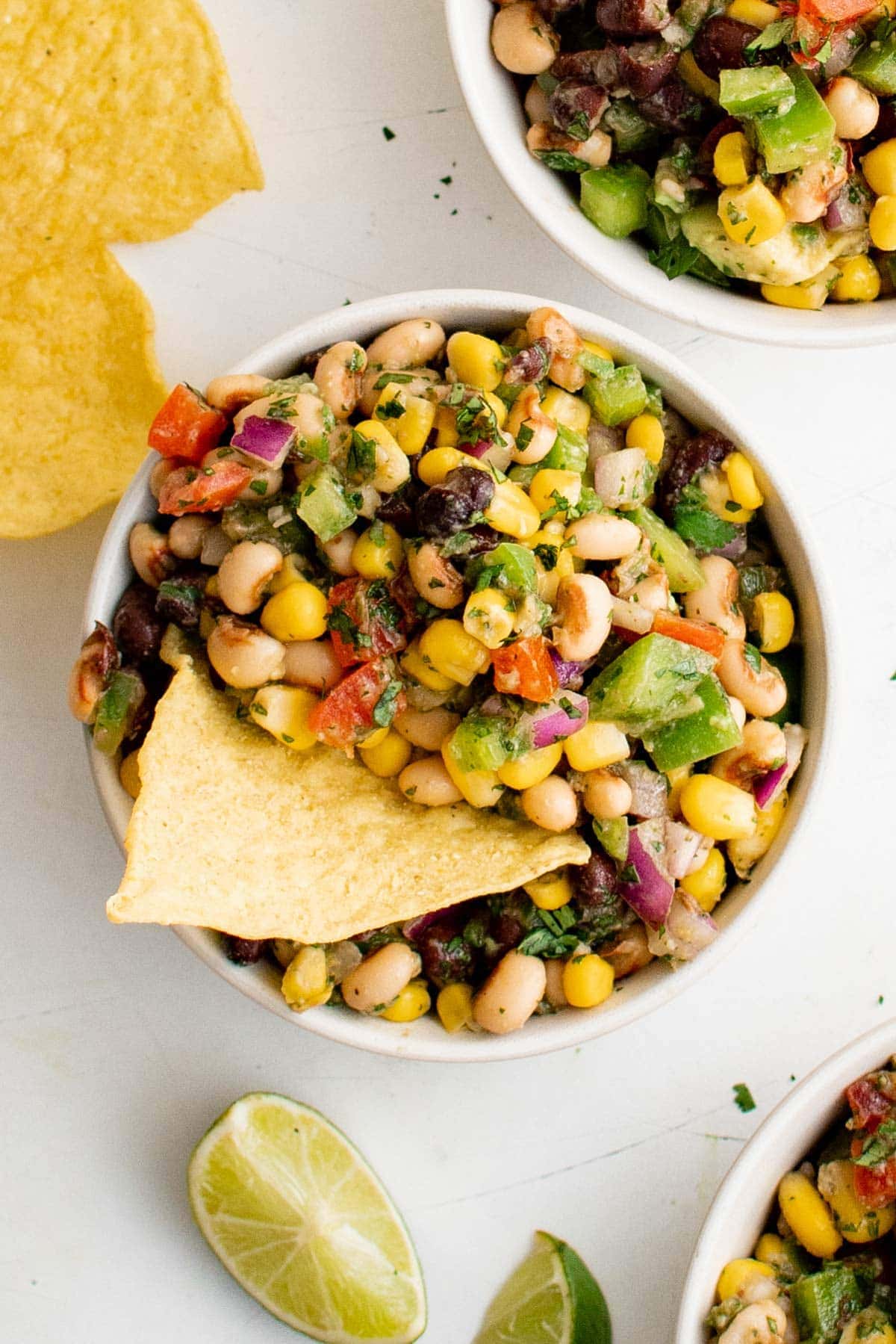 Three bowls with cowboy caviar salad in white bowls and tortilla chips.