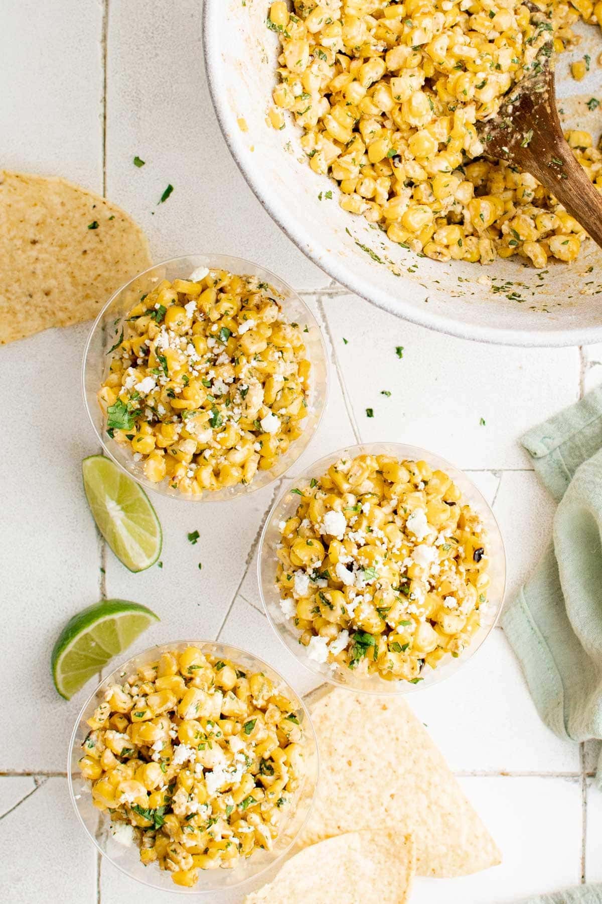 Corn salad in cups with tortilla chips and limes.