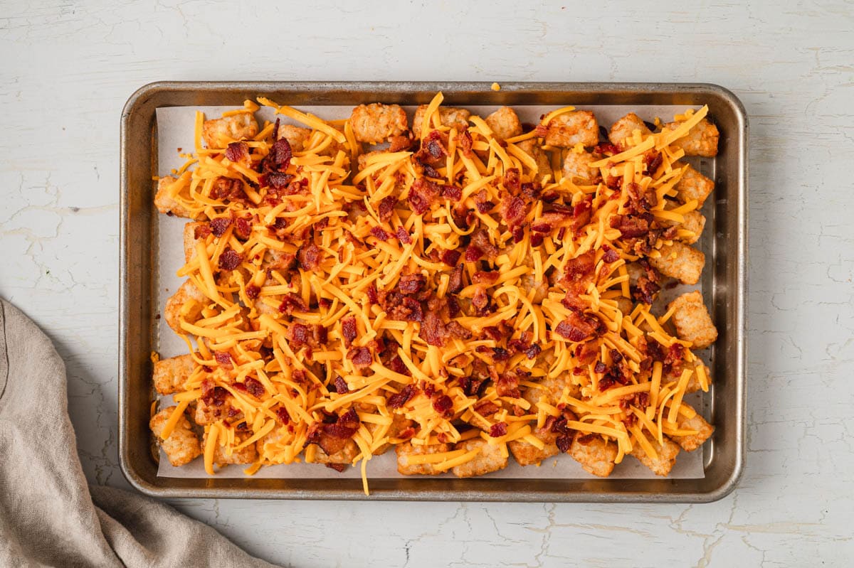 tater tots on a baking sheet with shredded cheese and crumbled bacon.