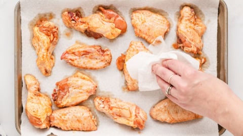 chicken wings on a baking tray with a hand patting dry with paper towel.