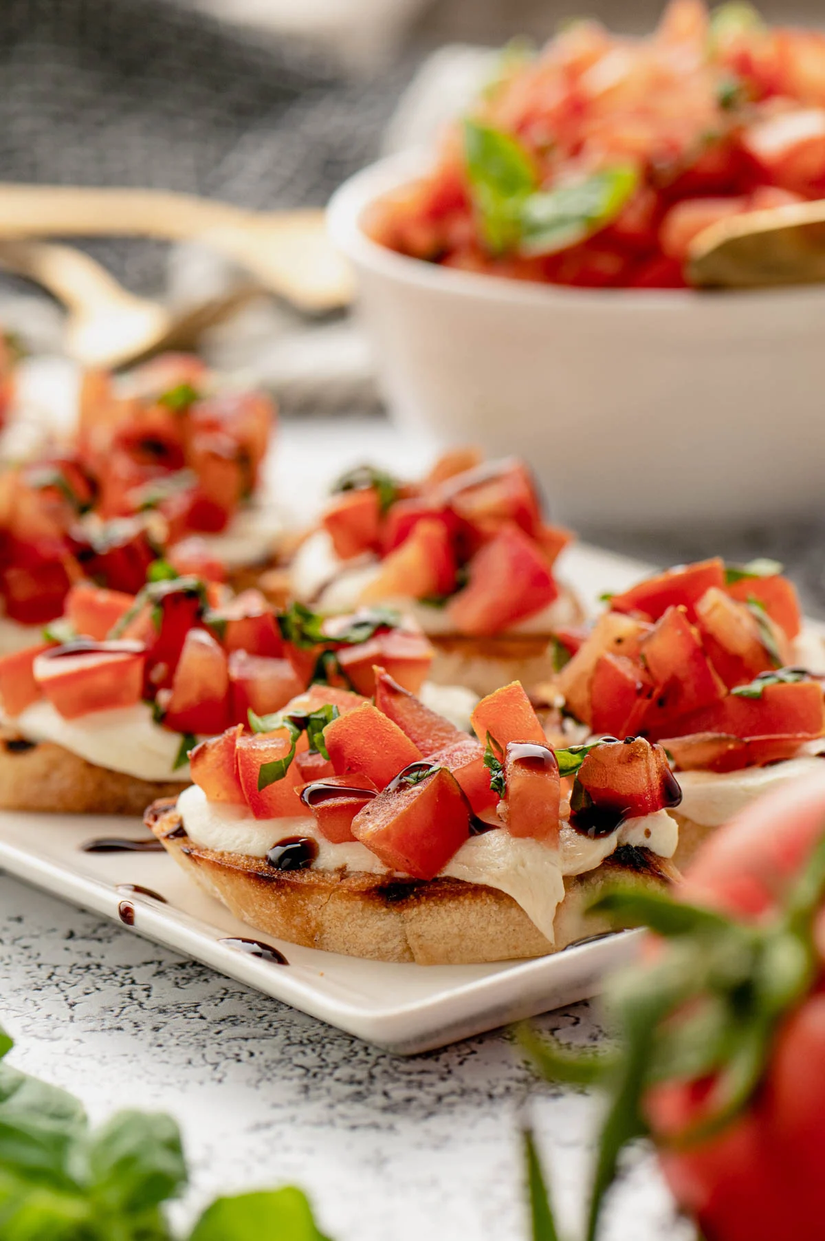 tomato mozzarella bruschetta on a platter with a bowl of tomatoes.