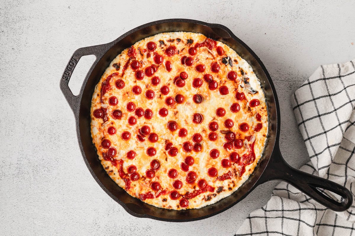Baked pizza dip with melted cheese and mini pepperoni on top in a cast iron pan.