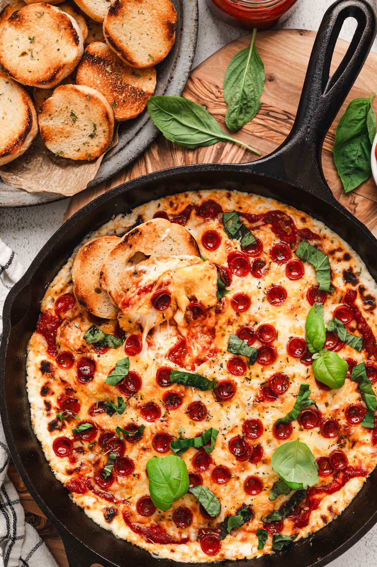 Pizza dip in a cast iron pan with two slices of toasted bread