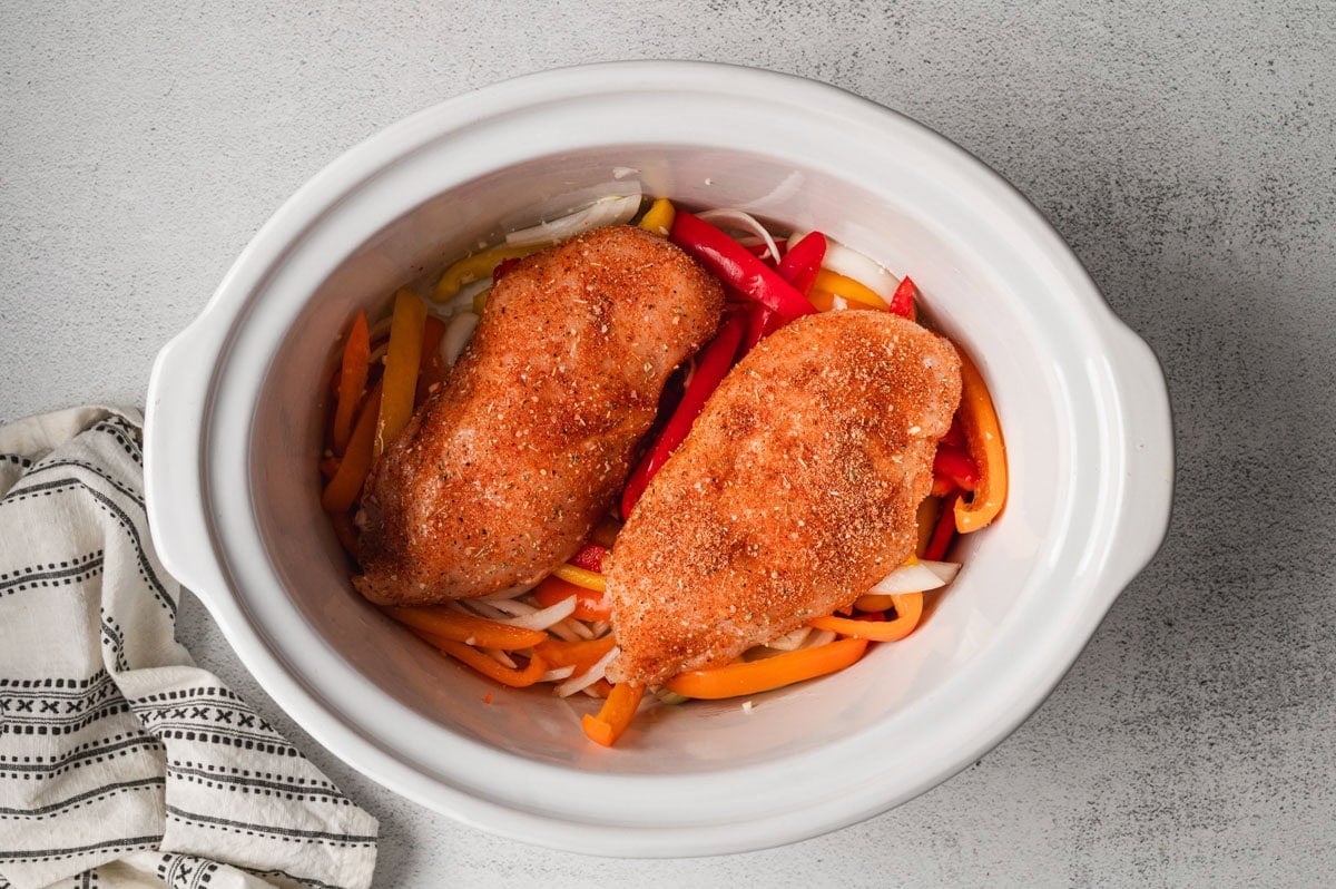 sliced pepper and raw chicken breasts in a slow cooker