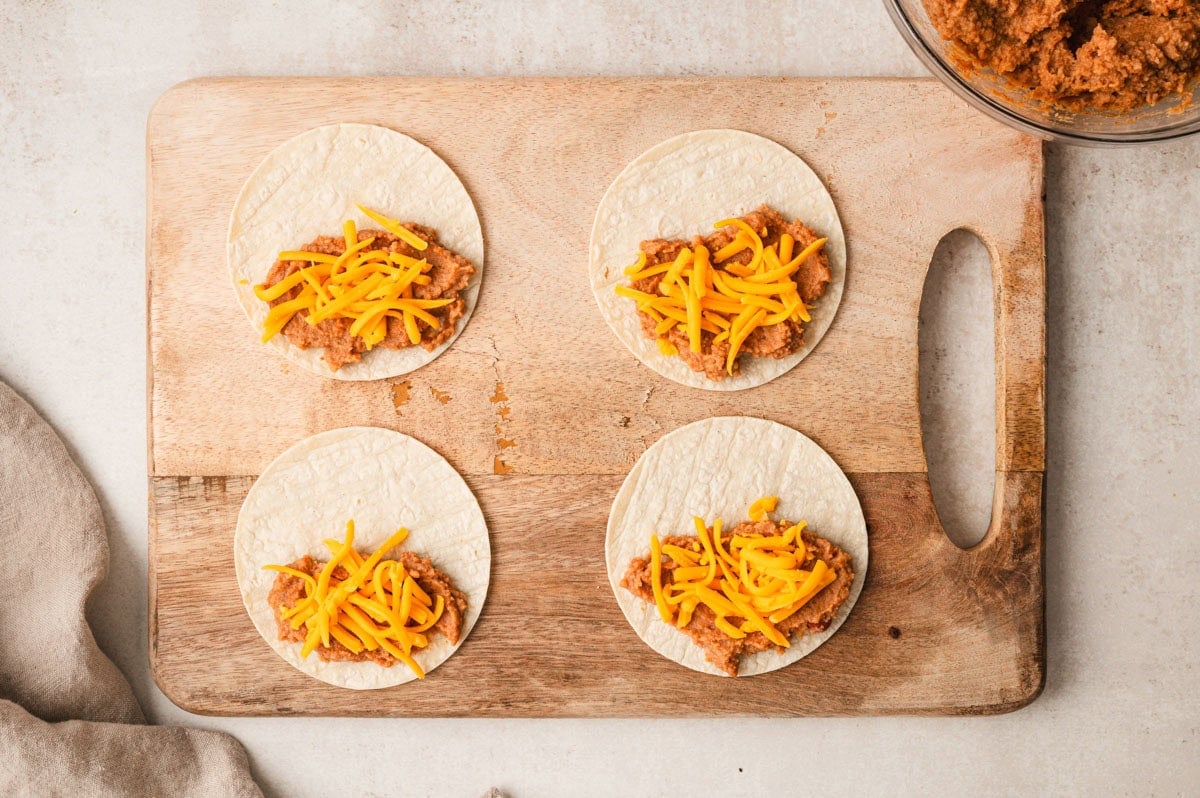 4 corn tortillas with refried beans and cheese on top.