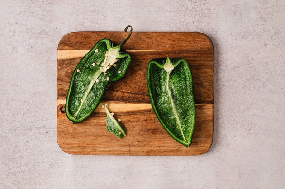 Poblano peppers cut in half on a wooden cutting board.