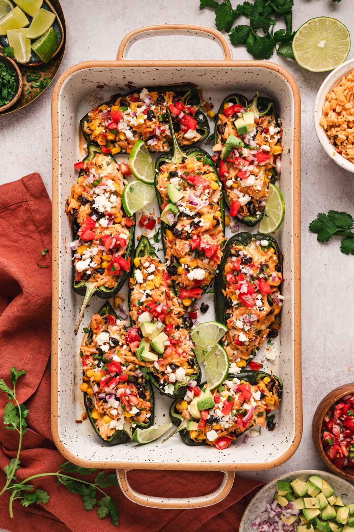 Chicken stuffed poblano peppers with lime wedges in a baking dish.