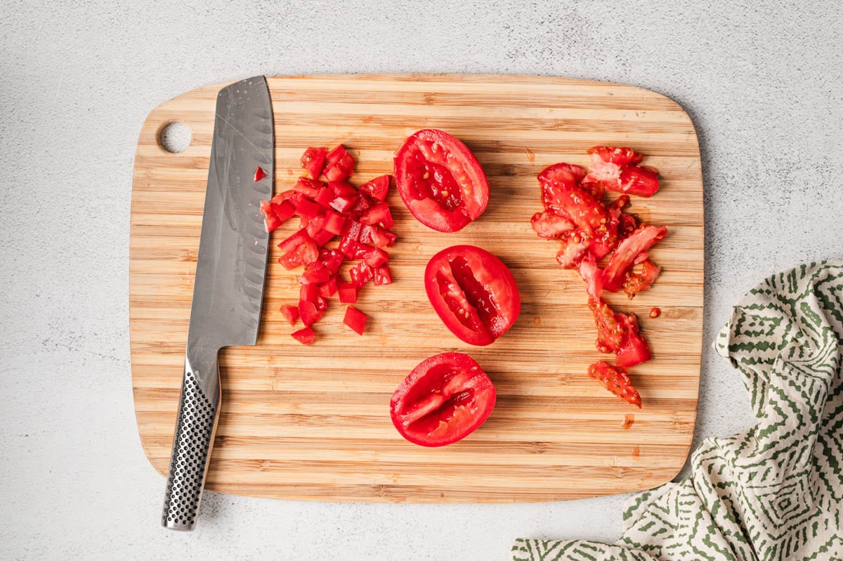 Tomatoes on a cutting board with the seeds removed in the process of being diced.