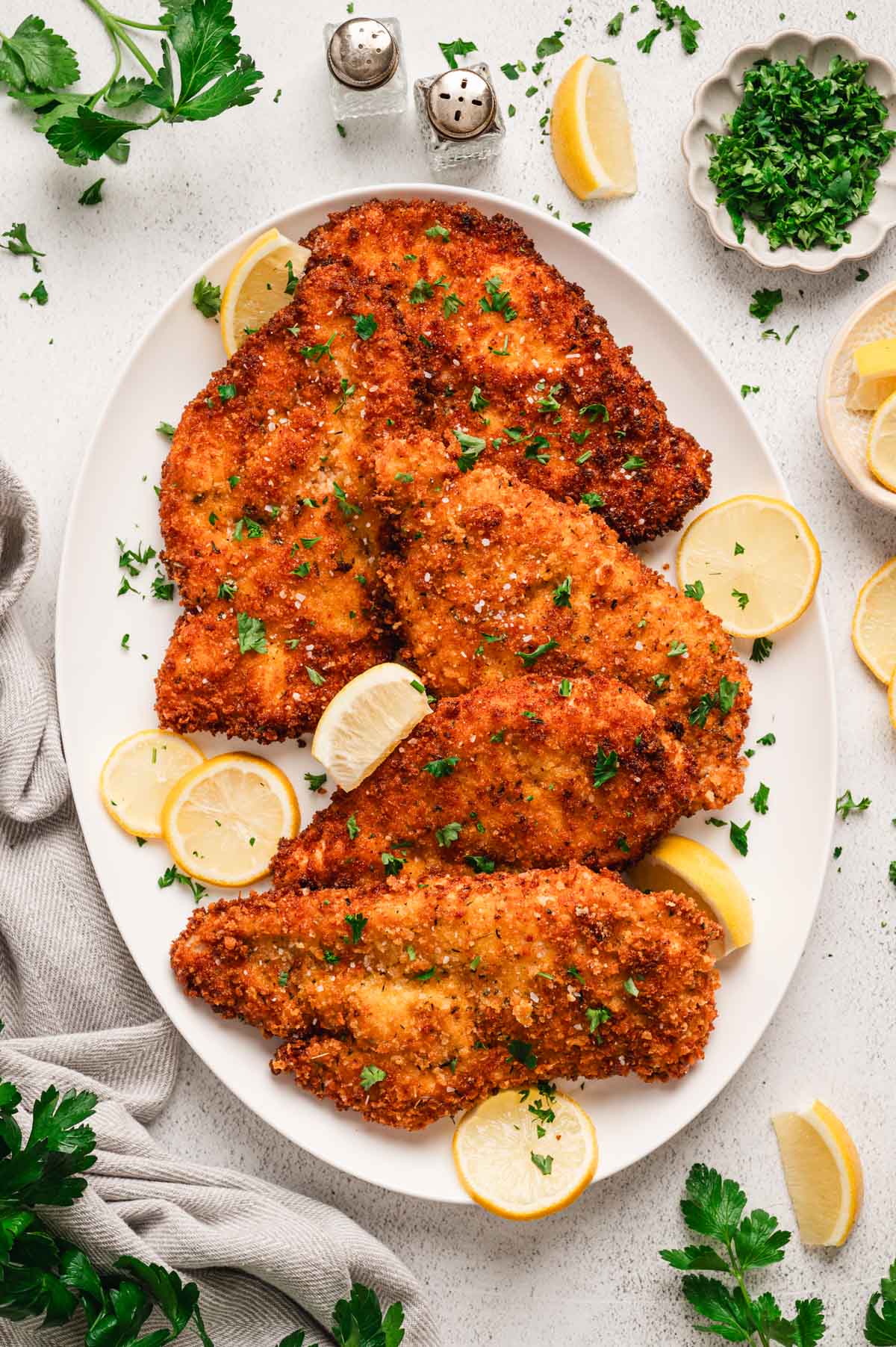 Crispy chicken cutlets on a white platter with lemon slices
