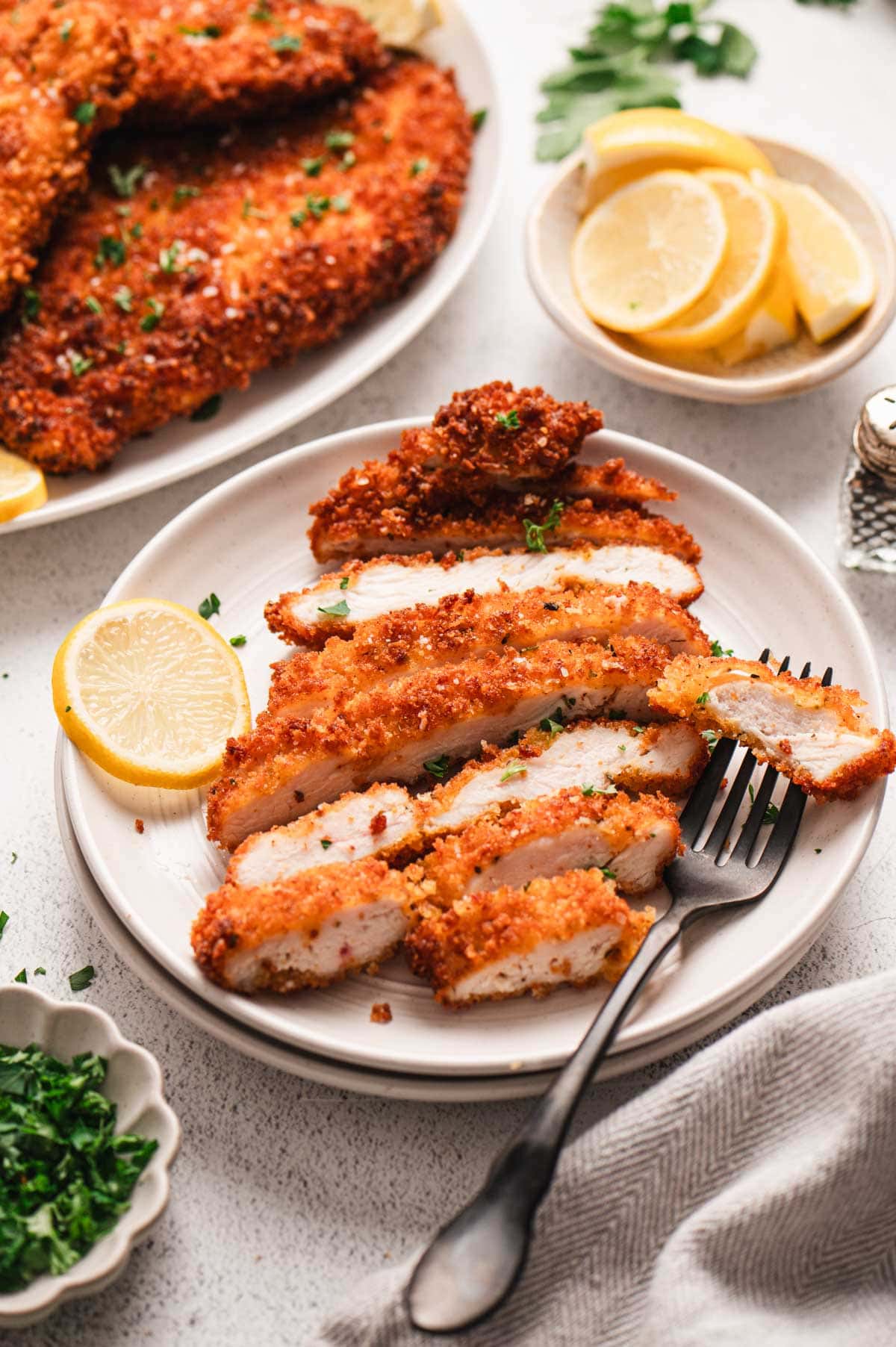 Sliced crispy chicken cutlet on a plate with fork and slice of lemon