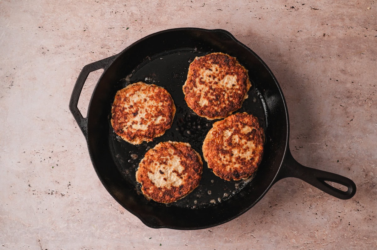 Chicken burger patties being cooked in a cast iron pan.