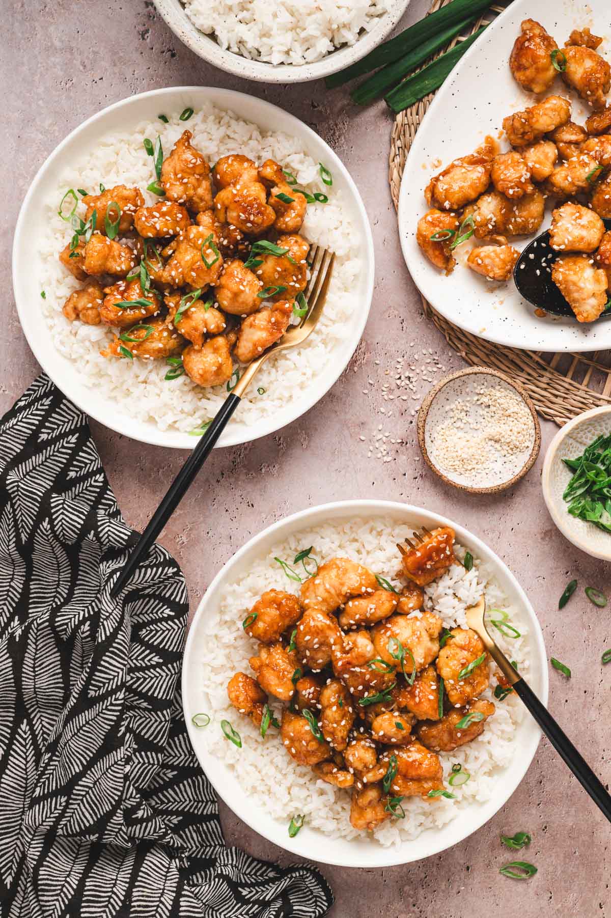 White plates with steamed white rice and sesame chicken and green onion garnish.