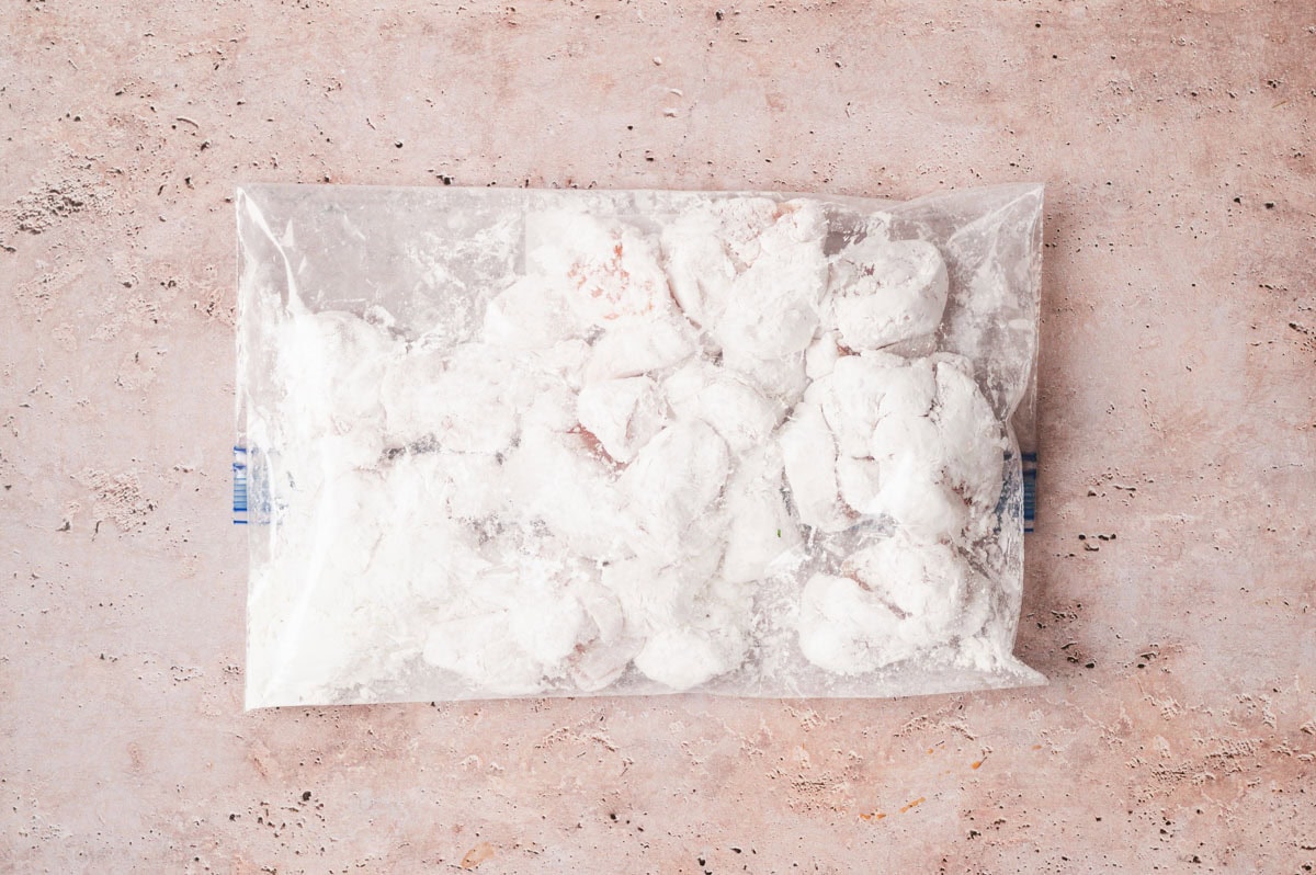 Chicken pieces coated in cornstarch in a plastic bag.