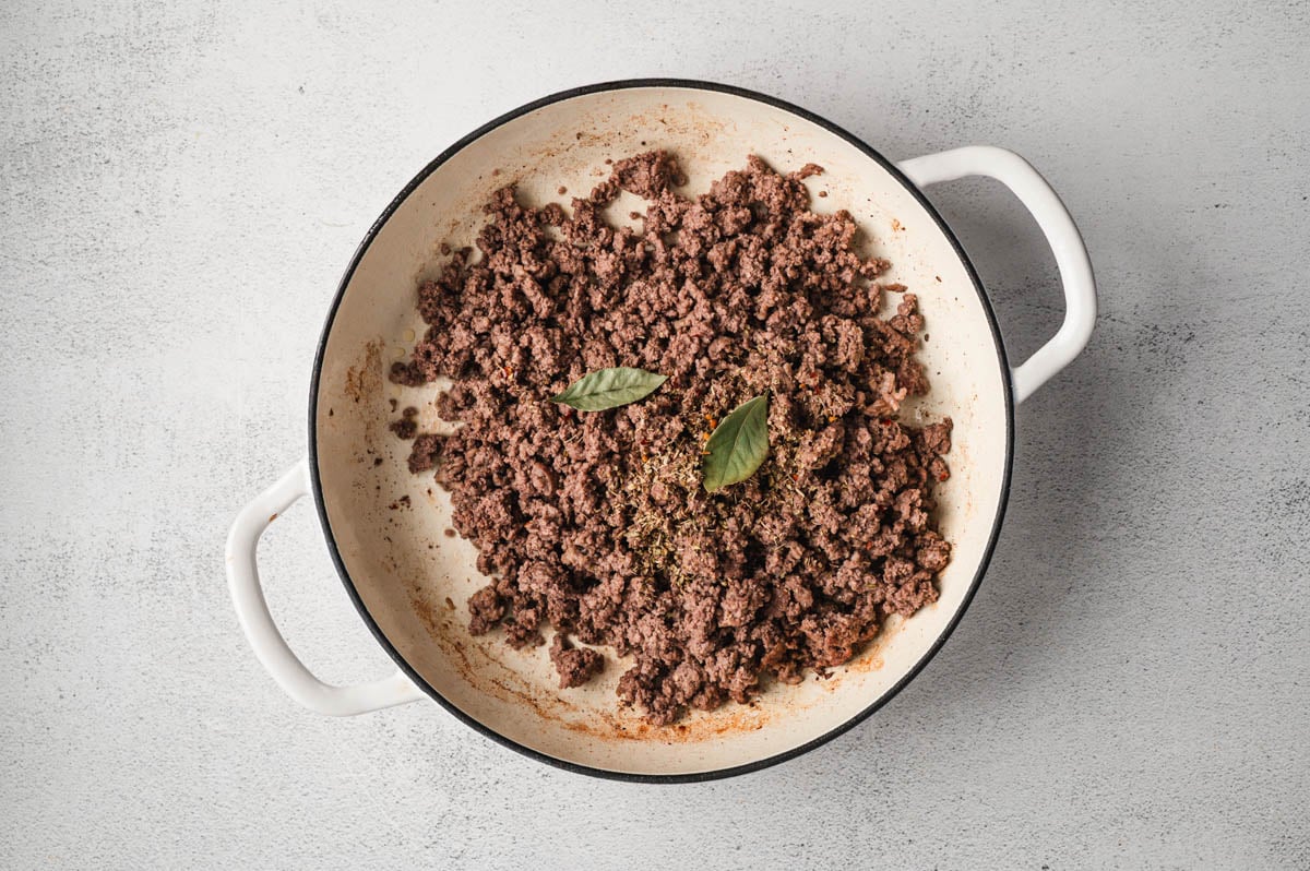 Cooked ground beef and Italian sausage in white enameled pot.