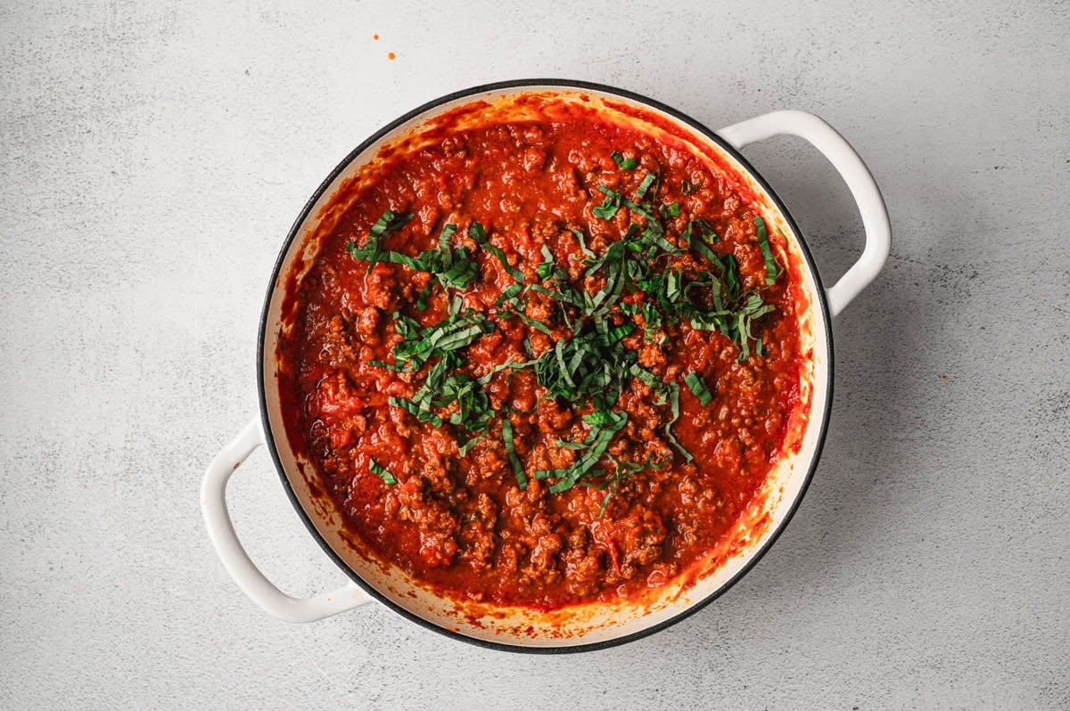Cooked marinara and meat sauce with fresh basil in a white pot.