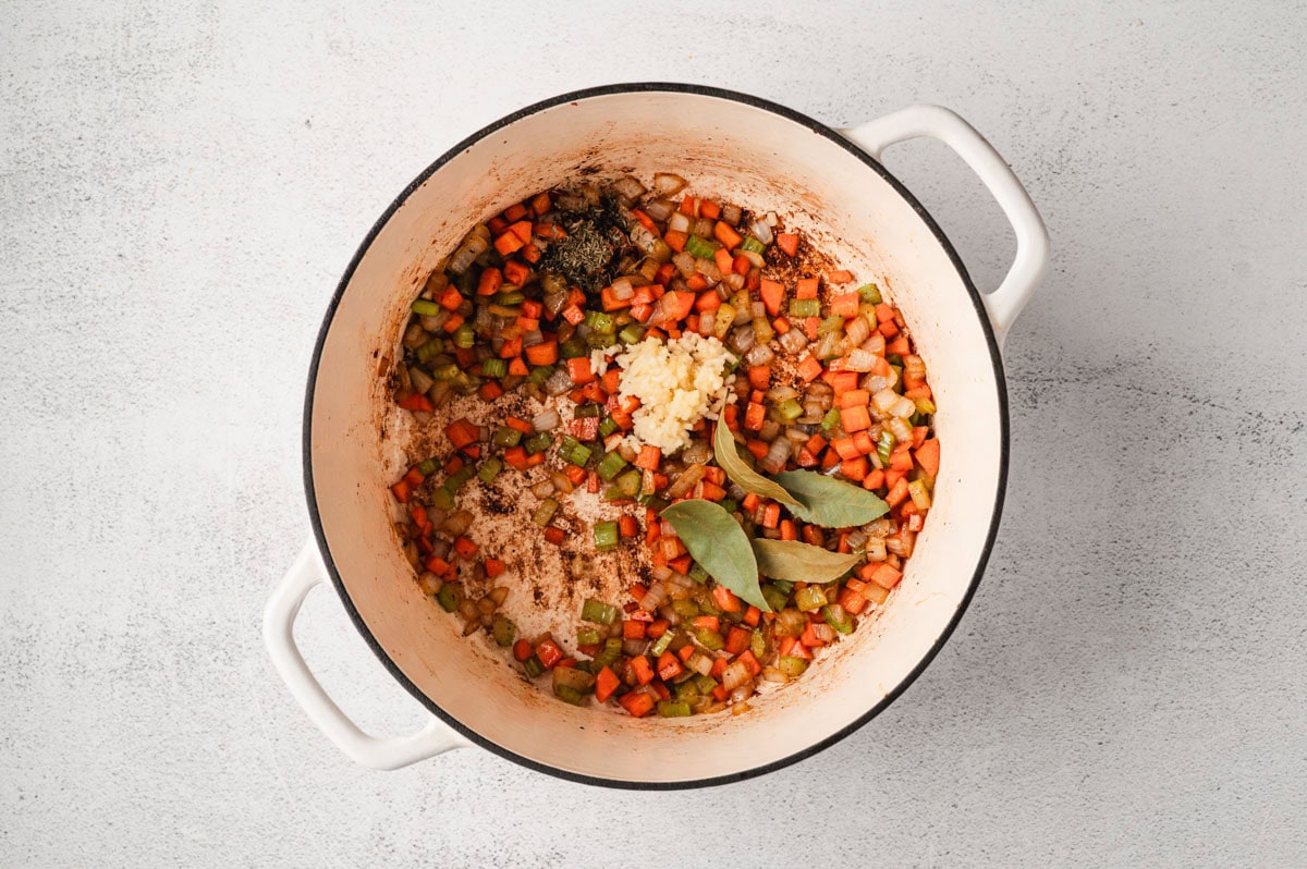 veggies and herbs for pea soup in a white enameled pot