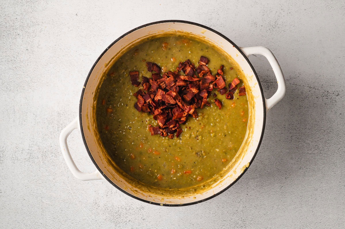 Cooked split pea soup with crispy bacon on top in a white enameled pot