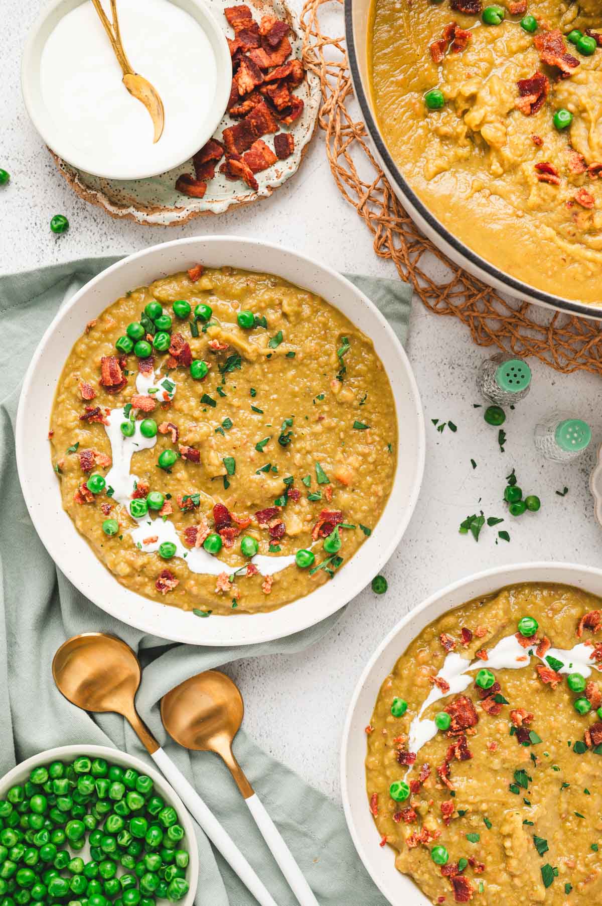 This Split Pea Soup Recipe with Bacon has a thick and creamy, split pea base, loaded with veggies, seasonings and tons of crunchy, salty bacon. Bowls of split pea soup with garnish of peas and bacon.