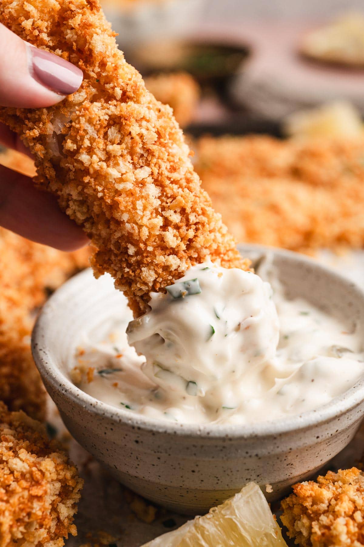 Fish stick dipped in a small dish of tartar sauce