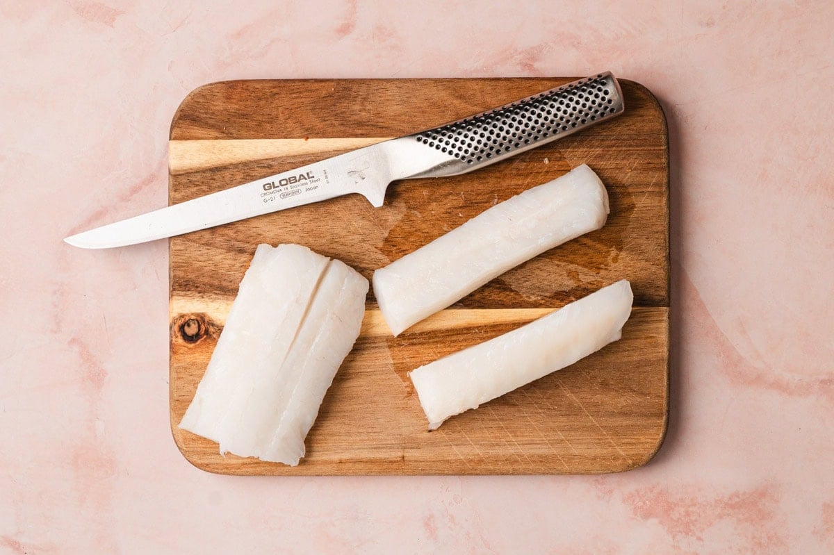 Pieces on cod on a cutting board with a knife.