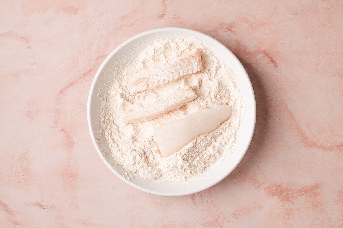 Pieces of cod in a dish with flour.