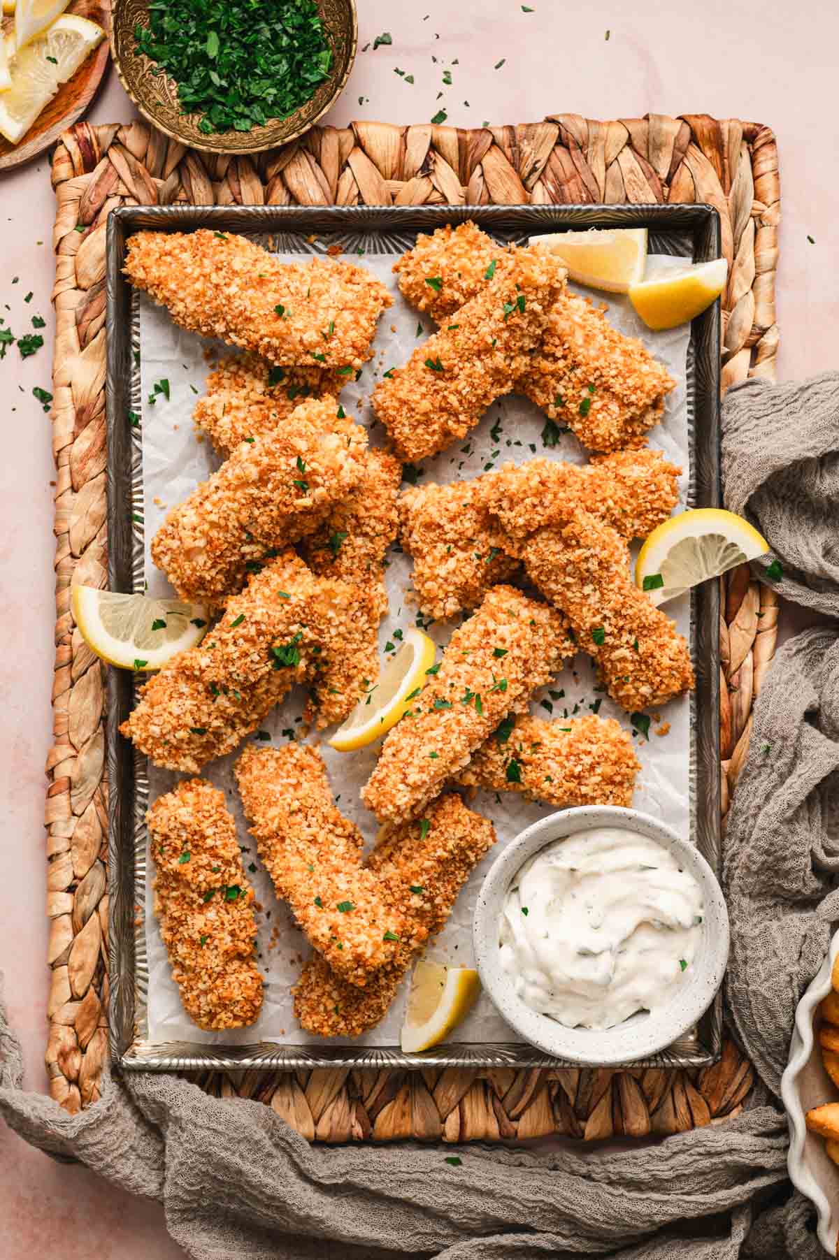 Baked fish sticks on a baking sheet with lemon wedges and tartar sauce.