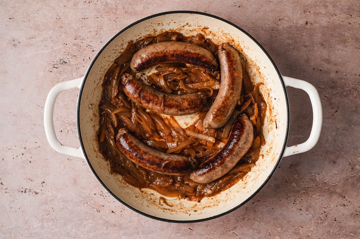 Sauteed onions and bratwurst sausages in a pan.