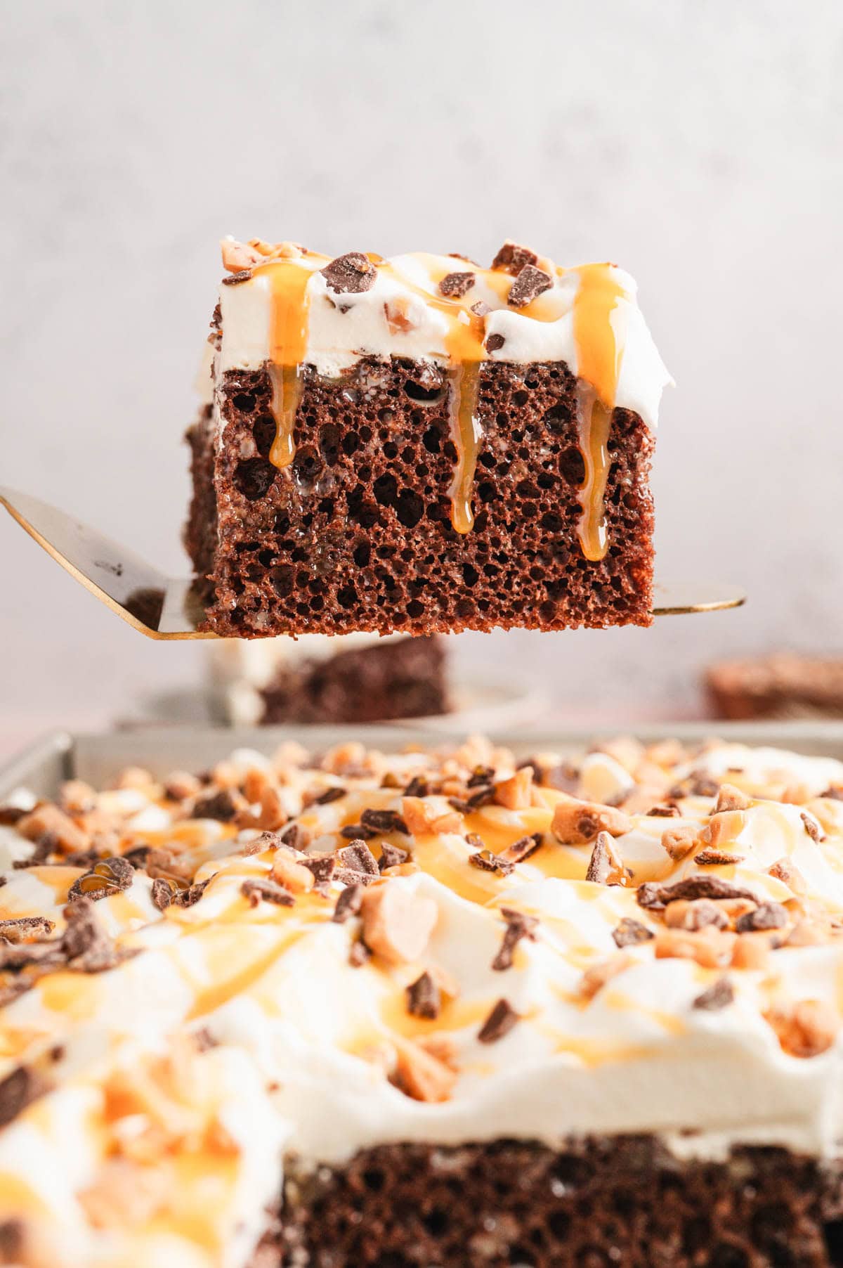 Slice of cake with whipped topping, caramel sauce and candy pieces on top.
