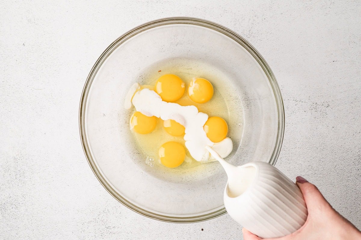 Eggs in a glass bowl with cream being poured in.