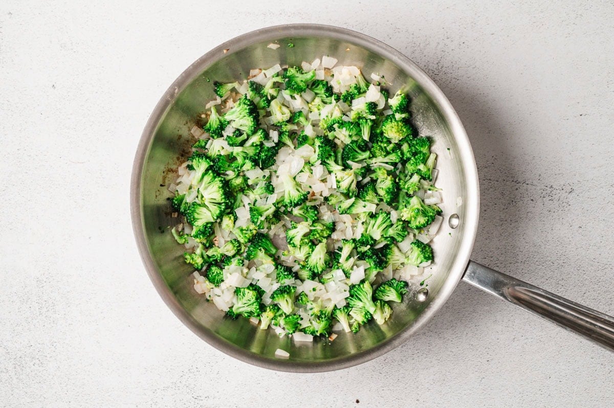 Broccoli and onions sauteing in a stainless steel pan.