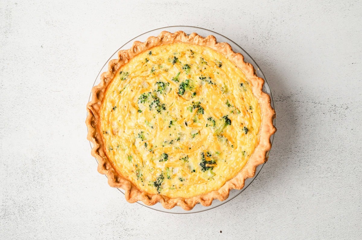 Baked broccoli cheddar quiche in glass pie dish.