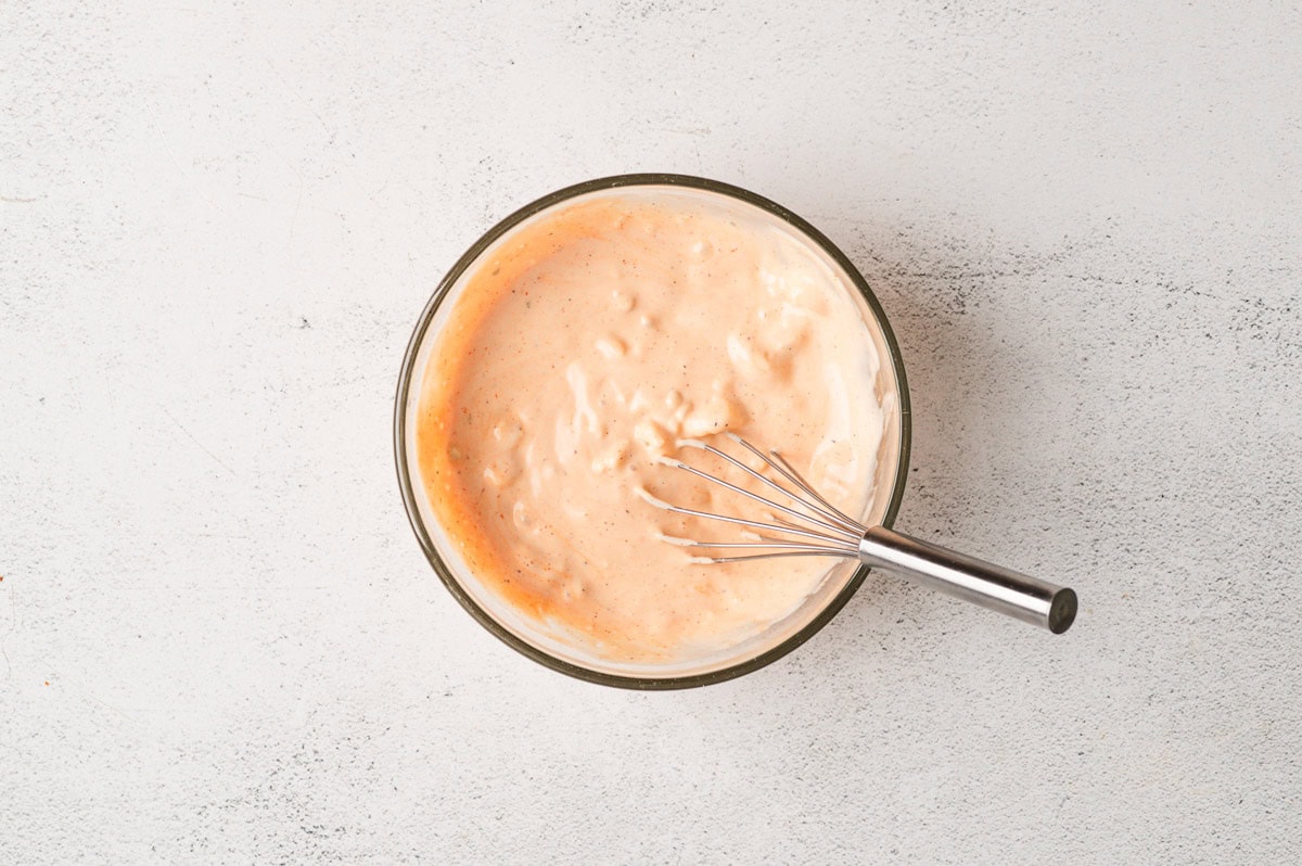 Sauce for buffalo chicken pasta salad in a glass bowl with a whisk.