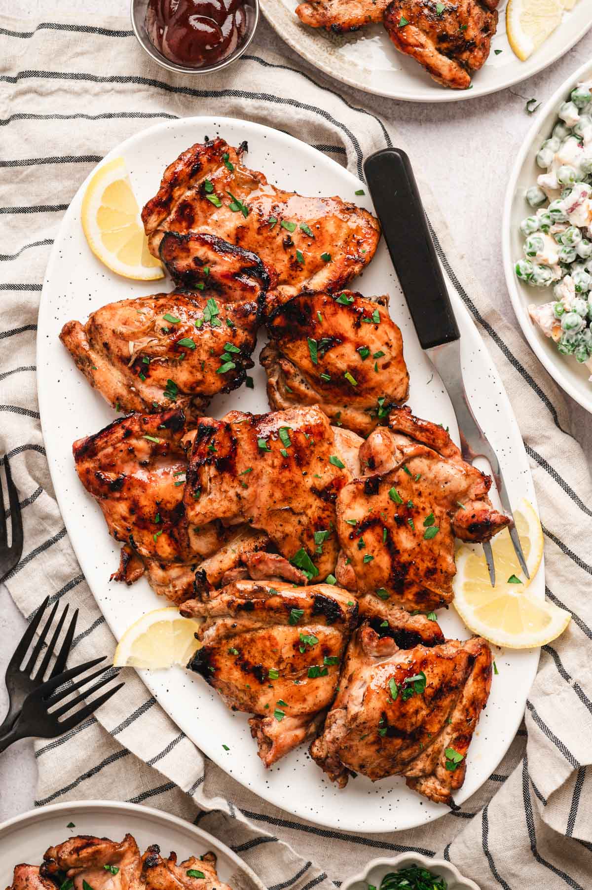 Grilled chicken thighs on a platter with a wedge of lemon.