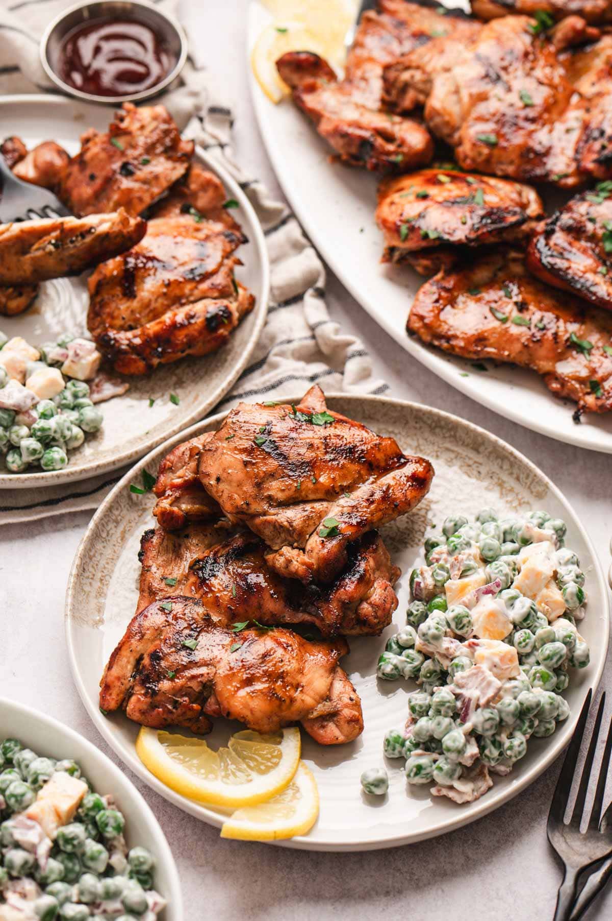 Grilled chicken thighs on a plate with pea salad and a wedge of lemon.