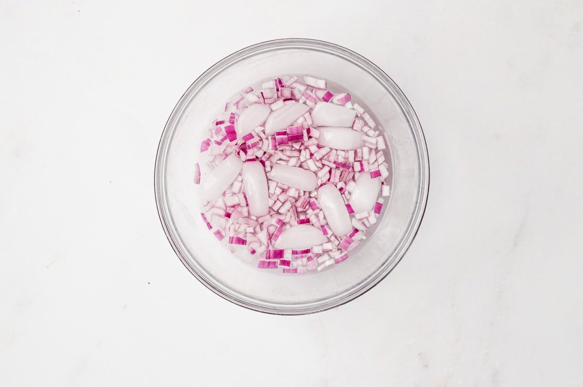 Diced red onion soaking in ice water in a glass bowl.