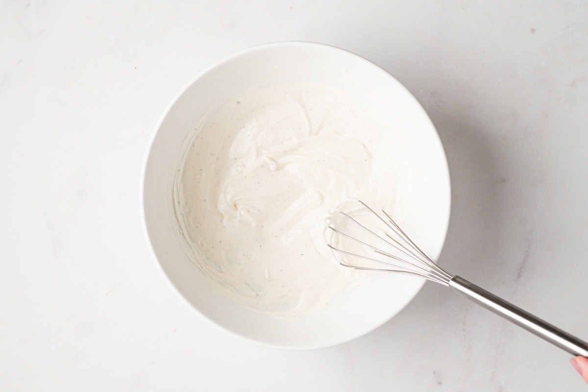 Creamy dressing and a stainless steel whisk in a white bowl.