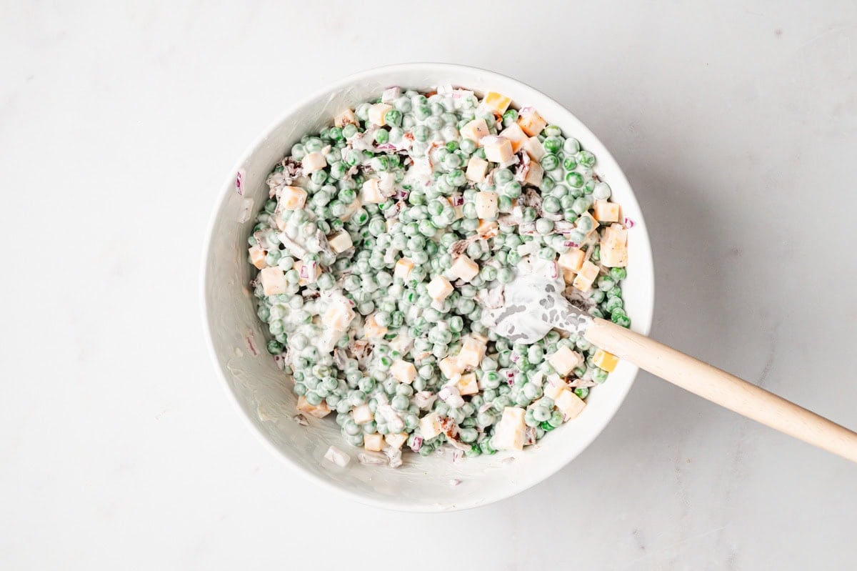 Pea salad with cheese, bacon, and onions covered in a creamy dressing in a white bowl.