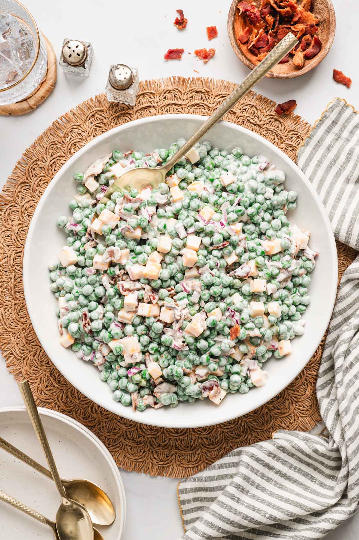 Pea salad with a creamy dressing, chunks of cheese, and diced bacon and onions in a white serving bowl.