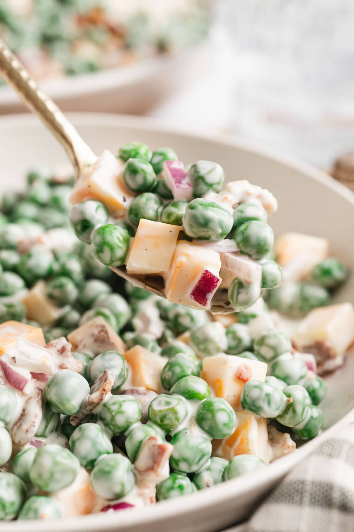 Close up of a spoon with pea salad, chunks of cheese and red onion.