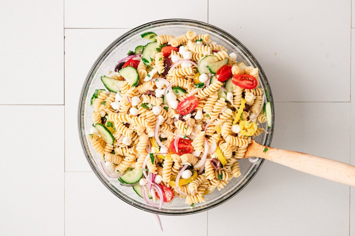 Pasta salad in a glass bowl with wooden spoon.