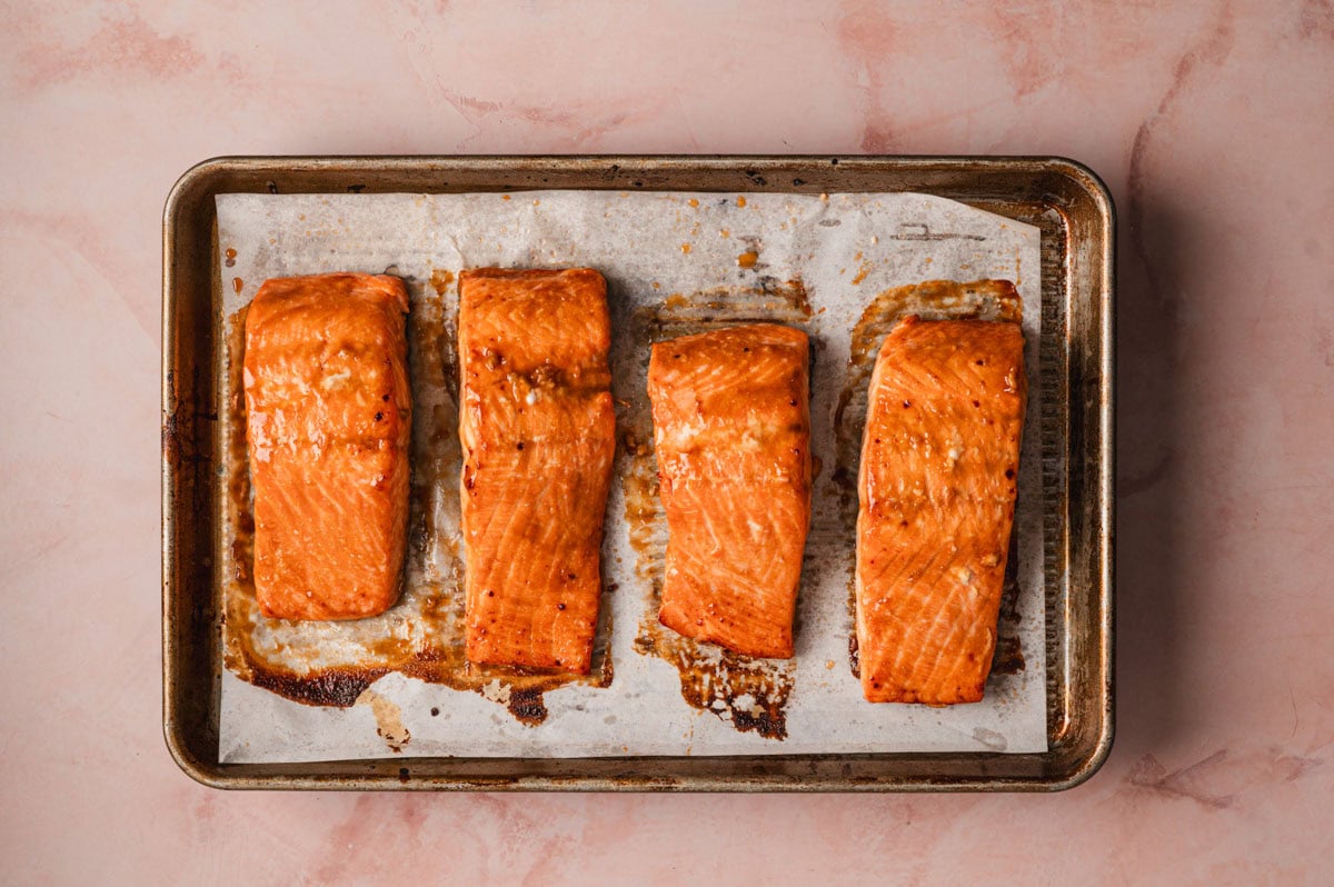 Four pieces of salmon cooked on a stainless steel baking sheet.
