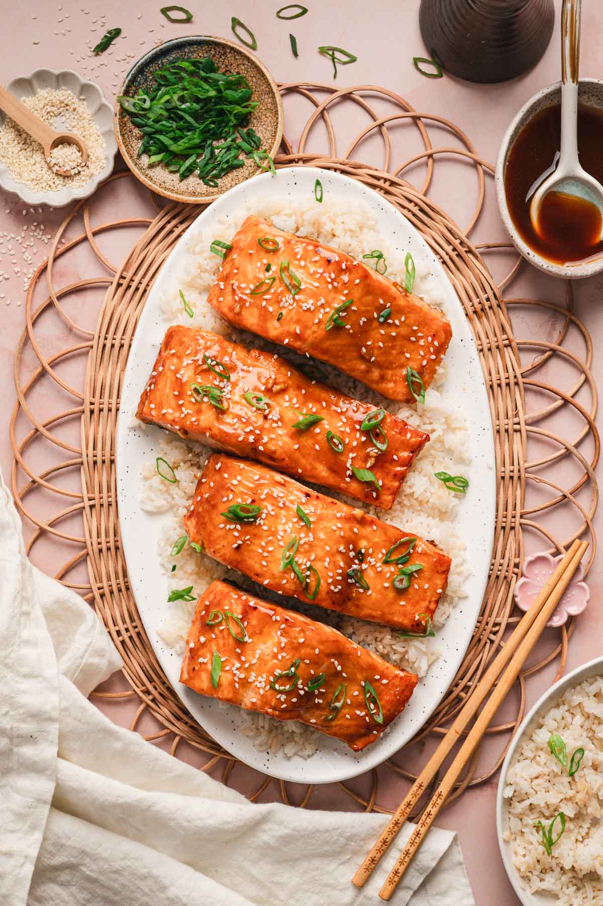 Four pieces of teriyaki glazed salmon topped with green onions and sesame seeds, all on a bed of white rice.