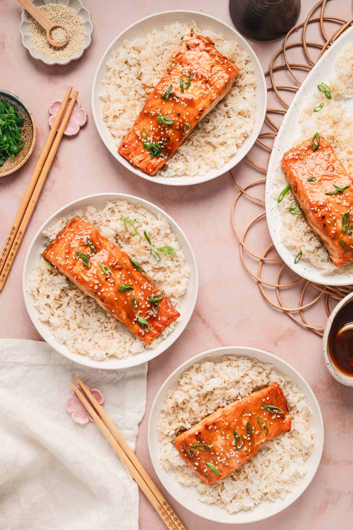 White bowls of rice and teriyaki glazed salmon topped with green onions and sesame seeds.